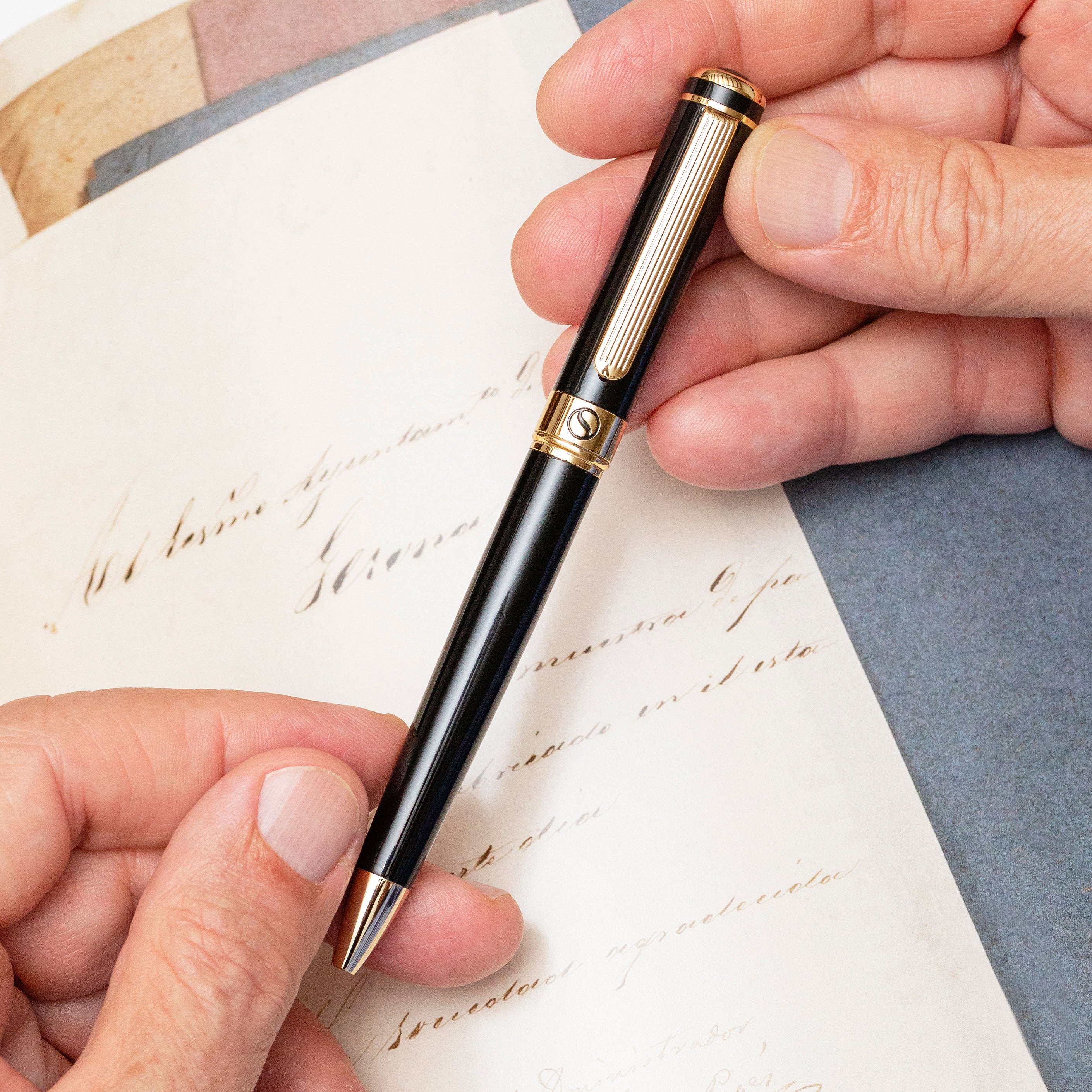 Hand holding a black and gold pen over a letter