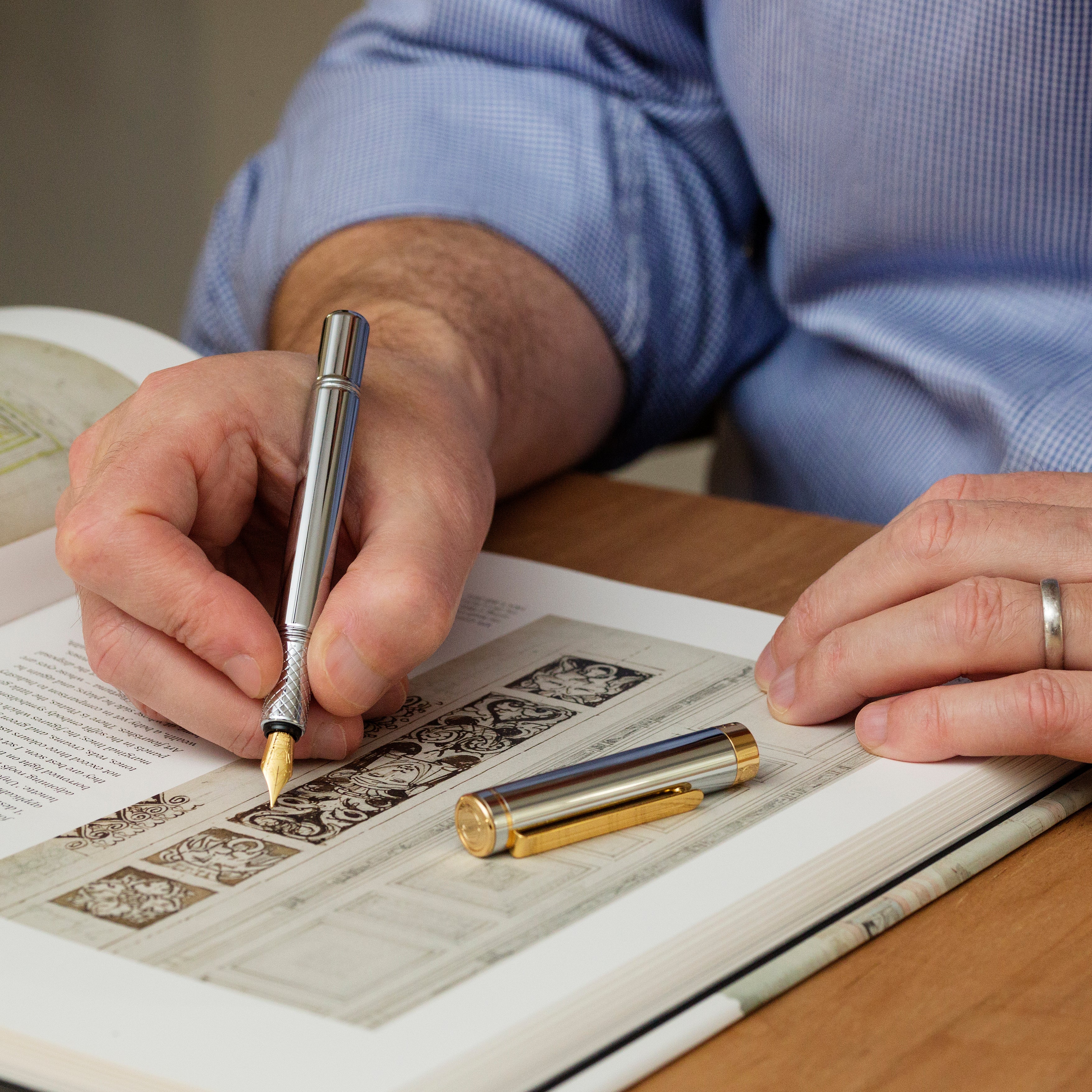 Person writing with a decorative pen on an open book
