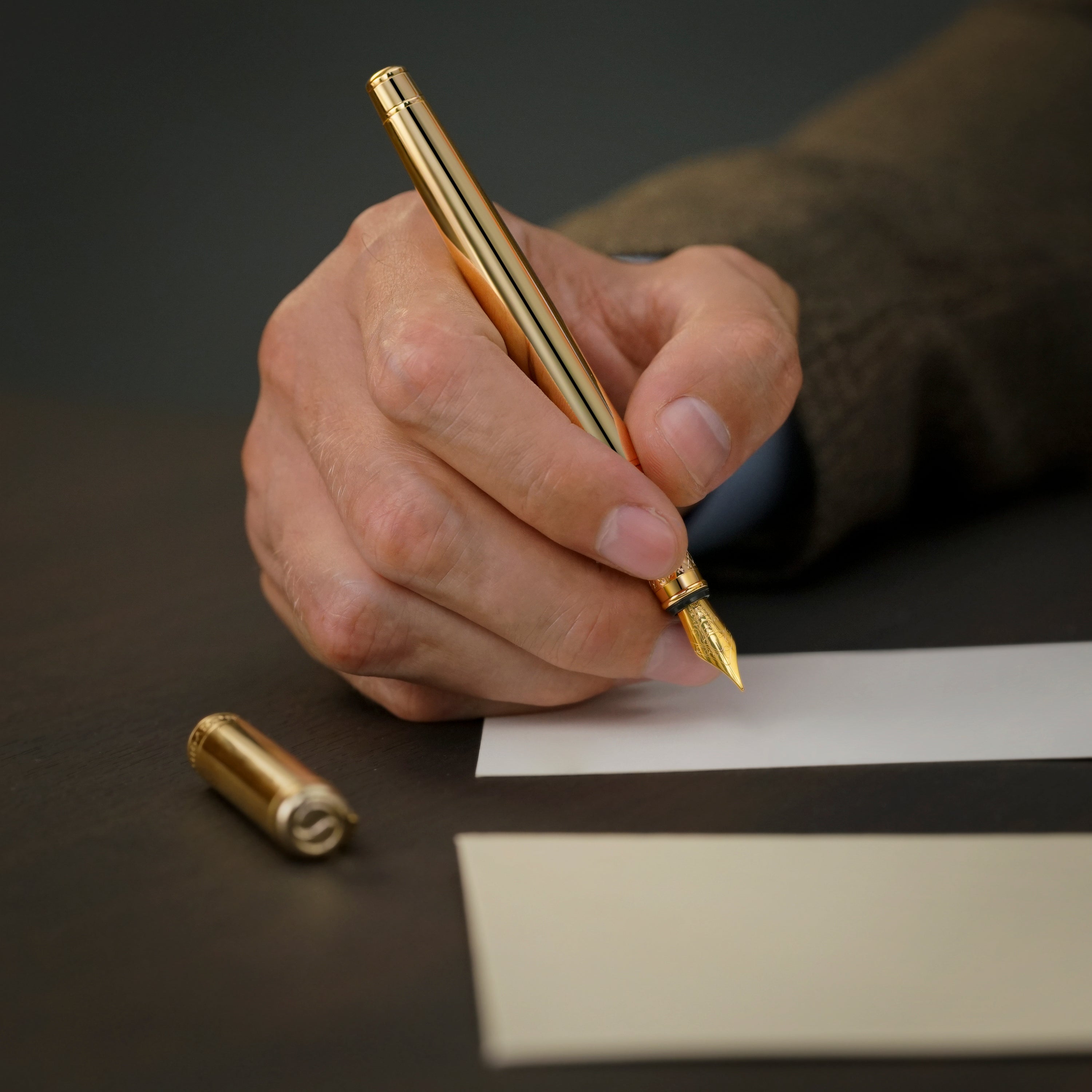 Hand holding a gold pen over paper with a dark background