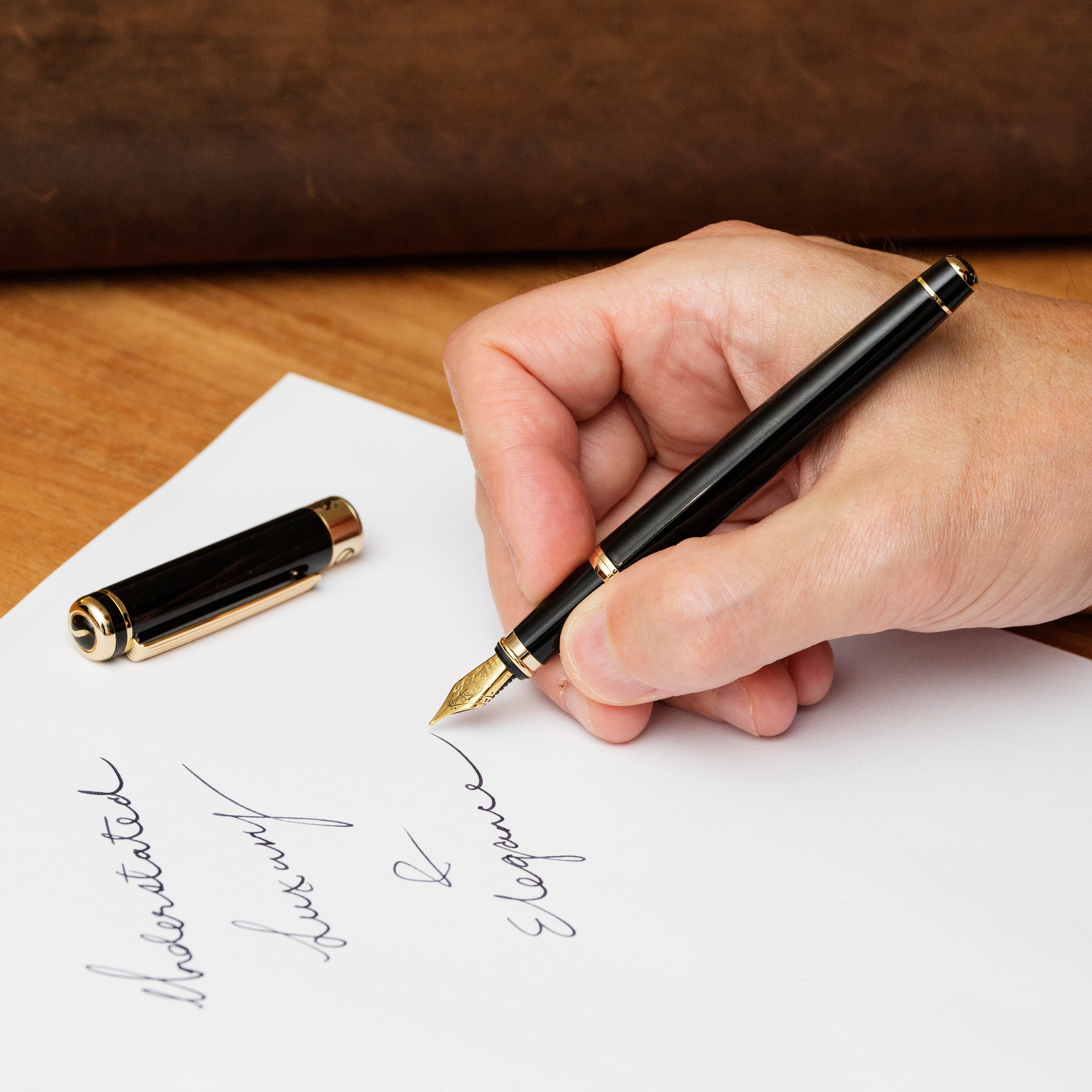 Hand writing on paper with a black fountain pen, close-up view.
